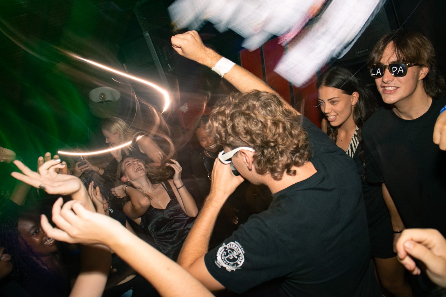 Crowd dancing at indoor event with blurry long exposure lighting.