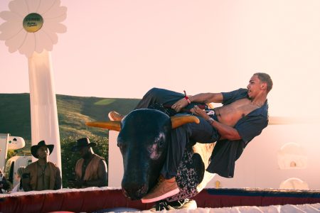 Man with open shirt hangs on to mechanical bull at music festival